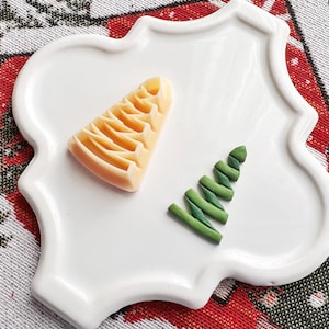 May include: A white ceramic plate with a scalloped edge features a green and a yellow tree-shaped cookie. The cookies are arranged on a white plate.