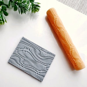 May include: A close-up of a gray textured rolling pin and a matching textured rubber stamp. The rolling pin is orange and the stamp is gray.