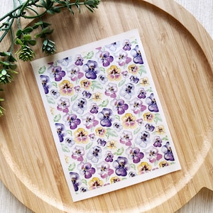 May include: A sheet of white paper with a repeating pattern of purple, yellow, and white pansies. The pansies are painted in a watercolour style.