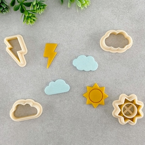 Könnte beinhalten: Ein Set mit acht Ausstechern in verschiedenen Formen, darunter Wolken, Blitze und eine Sonne. Die Ausstecher sind aus hellbeigefarbenem Kunststoff.