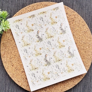 Pode incluir: Uma folha de papel branco com um padrão repetido de coelhos de aquarela em um campo de flores. Os coelhos são brancos com detalhes cinza e estão em várias poses.