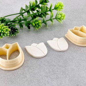 May include: Three white plastic tulip-shaped cookie cutters and one beige plastic tulip-shaped cookie cutter with a detailed design.