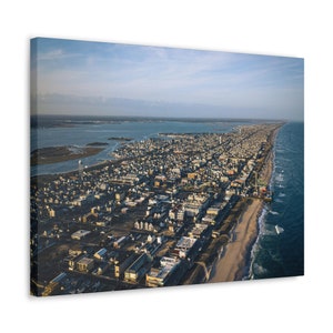 May include: An aerial view of a coastal town with a long sandy beach and blue ocean. The town is densely populated with houses and buildings. The beach is lined with a boardwalk and a pier.