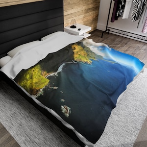 May include: A white duvet cover with a printed image of a green and brown cliffside overlooking a blue ocean. The ocean is a deep blue with white waves crashing on the shore. The sky is a light blue with white clouds.