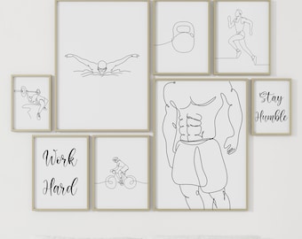May include: A set of eight black and white line art prints featuring motivational quotes and fitness-related imagery. The prints are framed in a light wood frame and are arranged on a white wall above a gray bed with white pillows. The prints include images of a person swimming, a person running, a person lifting weights, a person riding a bicycle, and a kettlebell. The quotes on the prints include "Work Hard" and "Stay Humble".