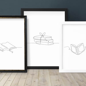 Puede incluir: Tres impresiones artísticas enmarcadas con dibujos lineales minimalistas de libros. Una muestra un libro abierto con un marcador, otra una pila de libros atados y la tercera un libro abierto. Los marcos son blancos y negros.