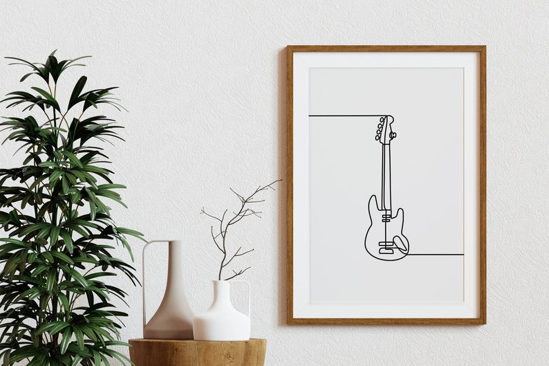 May include: A framed print of a line drawing of a bass guitar in black on a white background. The frame is brown wood.