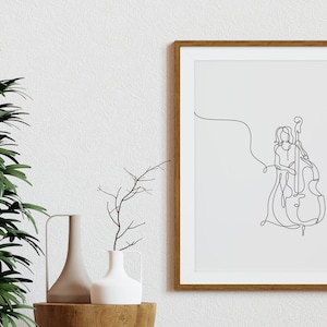 May include: A framed black and white line drawing of a person playing a double bass. The drawing is on a white background and is framed in a light brown wood frame.
