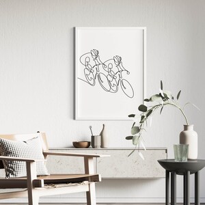 May include: A black and white line drawing of two cyclists riding bicycles. The drawing is framed and hanging on a white wall.