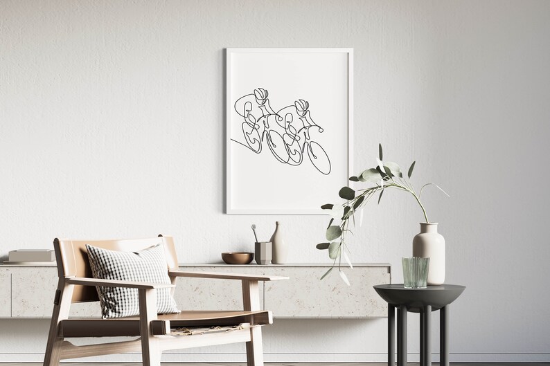 May include: A black and white line drawing of two cyclists riding bicycles. The drawing is framed and hanging on a white wall.
