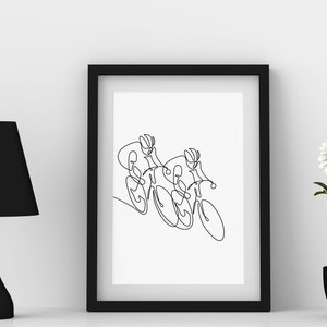 May include: A black framed print featuring a line drawing of two cyclists riding alongside each other. The print is displayed on a white wall, accompanied by a black lamp and a potted white flower.