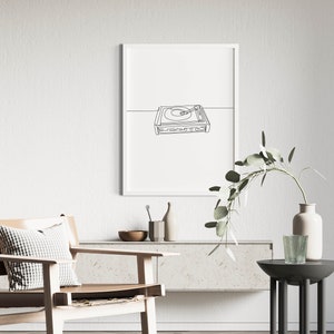 K&ouml;nnte beinhalten: Eine Schwarz-Wei&szlig;-Zeichnung eines Plattenspielers auf wei&szlig;em Hintergrund in einem wei&szlig;en Rahmen. Die Zeichnung h&auml;ngt an einer wei&szlig;en Wand &uuml;ber einem hellbraunen Holzregal mit einem hellbraunen Ledersessel mit einem schwarz-wei&szlig; karierten Kissen.