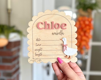 May include: A wooden sign with a scalloped edge and a pink goose design. The sign says "Chloe arabella" and has spaces to fill in the date, time, weight, and length.
