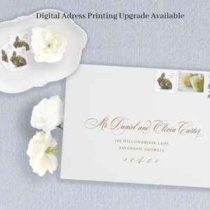 May include: A white envelope addressed to Mr. Daniel and Olivia Carter with gold calligraphy, featuring three postage stamps depicting a rabbit, roses, and a bird. A white scalloped dish holds additional rabbit stamps and white flowers.