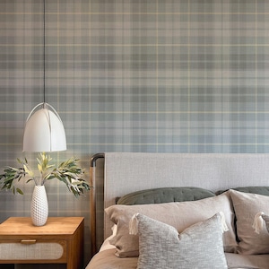 May include: A bedroom with a gray headboard bed, a green and gray plaid wallpaper, a white pendant light, a wooden nightstand, and a vase with green branches.
