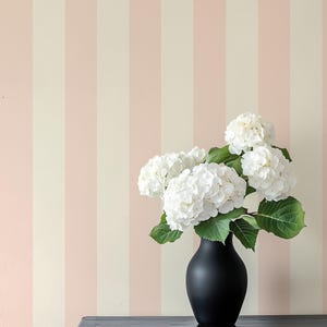 May include: A bouquet of white hydrangeas in a black vase on a black table against a pink and white striped wall.
