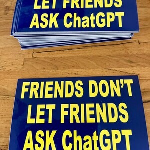May include: A stack of blue rectangular stickers with yellow text that reads "FRIENDS DON'T LET FRIENDS ASK ChatGPT". The stickers are on a wooden surface.