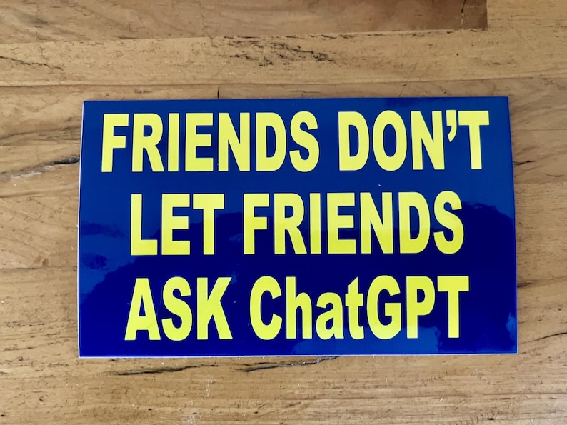 May include: A rectangular blue sticker with yellow text that reads: "FRIENDS DON'T LET FRIENDS ASK ChatGPT". The sticker is on a wooden surface.