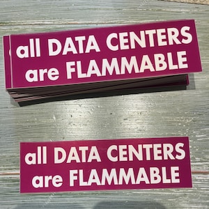 May include: A stack of magenta rectangular stickers with the text "all DATA CENTERS are FLAMMABLE" in white. One sticker is separate and visible below the stack. The stickers are on a light gray surface.