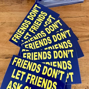 May include: A stack of blue rectangular stickers with yellow text. The text on the stickers reads "FRIENDS DON'T LET FRIENDS ASK ChatGPT". The stickers are arranged on a wooden surface.