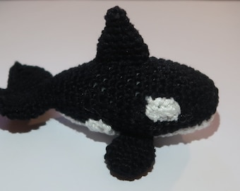 May include: A handmade crochet orca whale toy. The toy is primarily black with white accents on the belly and sides. It has a dorsal fin and a tail fin. The toy is likely stuffed with soft material.