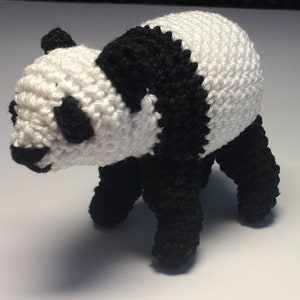 May include: A crocheted panda bear toy with black and white fur. The panda is standing on all fours and has a cute expression.