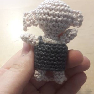 May include: A small crocheted amigurumi toy in the shape of a creature with a gray vest and white body.