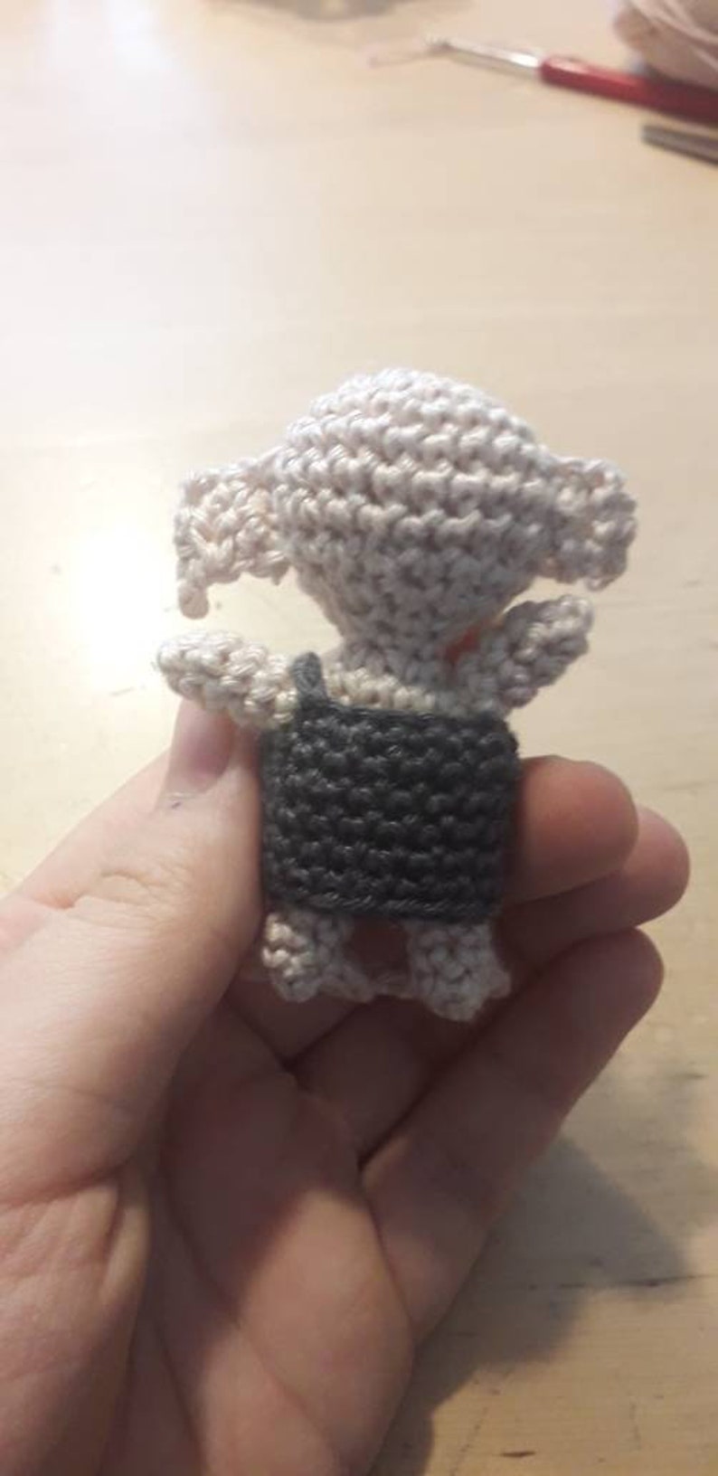 May include: A small crocheted amigurumi toy in the shape of a creature with a gray vest and white body.