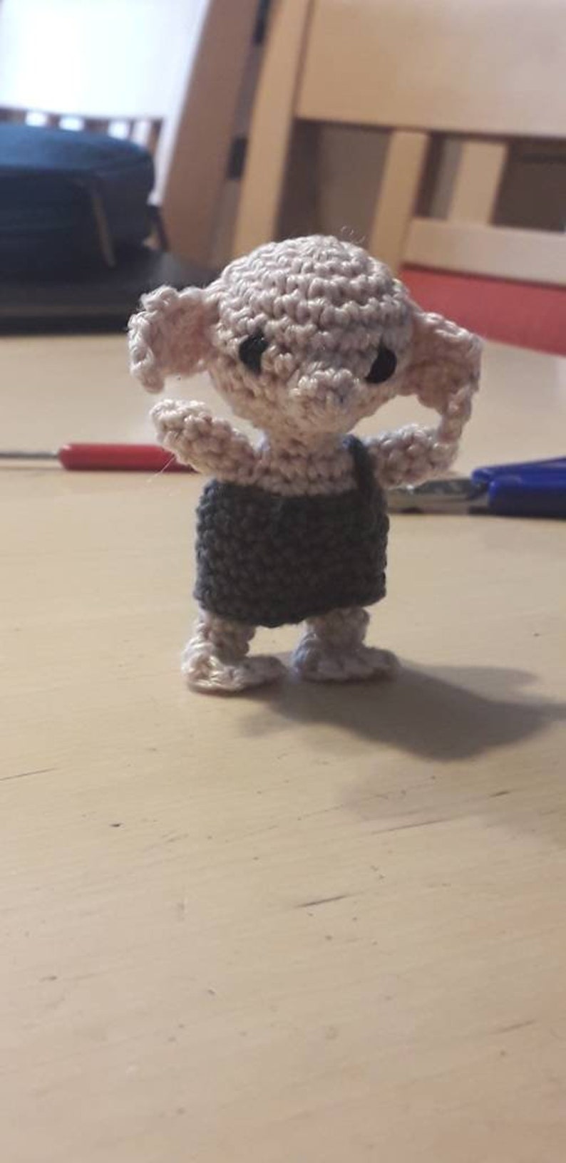 May include: A crocheted Dobby doll with a gray and white outfit. The doll has large ears and black eyes.