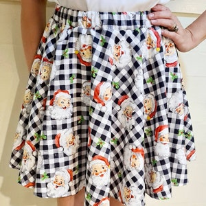May include: A black and white gingham skirt with a festive print of Santa Claus faces. The skirt has a wide elastic waistband and a flared silhouette.
