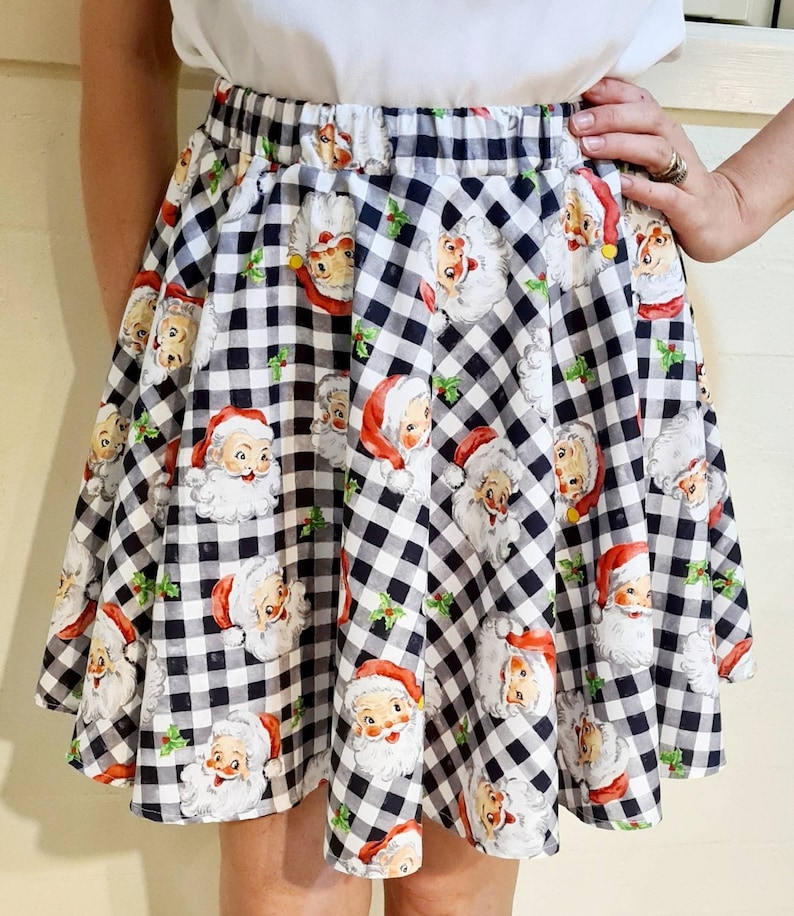 May include: A black and white gingham skirt with a festive print of Santa Claus faces. The skirt has a wide elastic waistband and a flared silhouette.