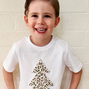 May include: A white t-shirt with a festive Christmas tree design. The tree is made of fabric with a green and red holly pattern.