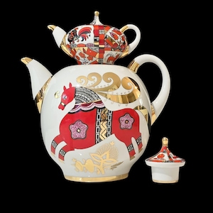 Könnte beinhalten: Eine weiße Porzellanteekanne mit gestapeltem Design, bei dem eine kleinere Teekanne oben aufsitzt. Der Körper ist mit einem roten Pferdemotiv, goldenen Schnörkeln und Blumenmustern verziert. Ein separater passender Deckel steht neben der Basis.