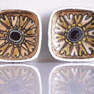 Puede incluir: Dos platos cuadrados de cerámica con un diseño floral. El centro de cada plato es de color granate oscuro, rodeado por un patrón floral amarillo y beige. Los bordes son blancos.