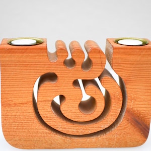 May include: A wooden candle holder with two brass-rimmed wells for candles. The orange-brown wood is carved with a decorative, flowing design. The candle holder is a unique home decor item.