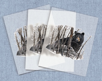 May include: A black bear stands in a snowy forest with bare branches. The bear is looking to the left of the image. The bear is in the foreground of the image. The background is a snowy forest with bare branches.