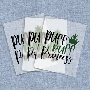 May include: Three translucent sheets with the words "Puff Princess" in a script font. The word "Puff" is repeated multiple times. A green crown with a cannabis leaf is on one sheet. The background is a light blue fabric.