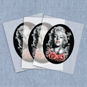 May include: Three black and white images of Marilyn Monroe with red roses and silver stars on a black background. The images are printed on clear sticker paper.