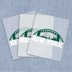 May include: Three white rectangular decals with a green football design and the words "NEW YORK" in white. The football design includes a silhouette of the New York City skyline. The decals are layered on a light blue textured background.