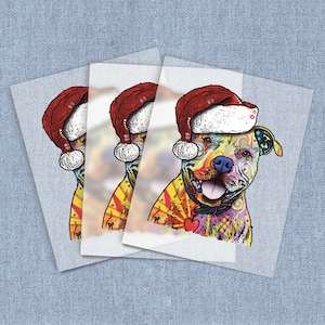 May include: Three layered prints featuring a colorful pit bull wearing a Santa hat. The dog has a vibrant design with red, yellow, blue, and green hues. A red heart is on the dog's collar. The background is a light blue denim texture.