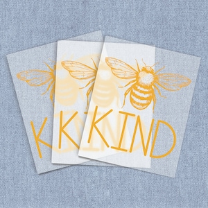 May include: A yellow and white graphic design with the word "KIND" in yellow letters and a stylized drawing of a bee with yellow wings.