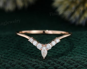 May include: A delicate rose gold wedding band with a marquise-shaped center stone and smaller round stones set in a V-shaped design.