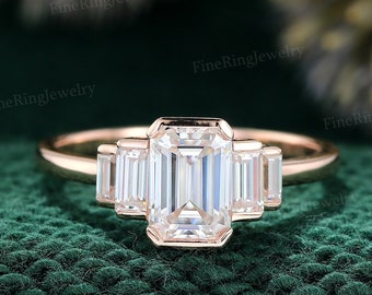 May include: A rose gold engagement ring with an emerald cut diamond center stone and three smaller baguette cut diamonds on each side.