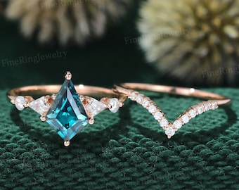 May include: A rose gold engagement ring set with a square emerald cut teal gemstone surrounded by smaller diamonds. The matching wedding band is a delicate rose gold band with a v-shaped row of diamonds.
