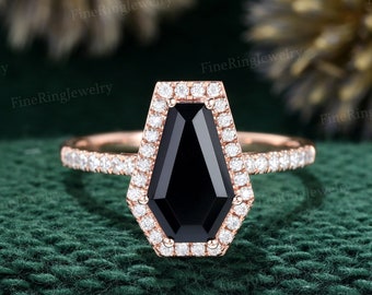 May include: A rose gold engagement ring with a black diamond in a coffin-shaped setting. The ring is surrounded by a halo of smaller diamonds.