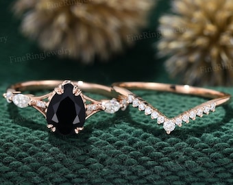May include: A pear-shaped black diamond engagement ring set in rose gold with a delicate diamond band. The engagement ring features a pear-shaped black diamond with a pave setting of smaller diamonds. The wedding band is a simple rose gold band with a row of diamonds.