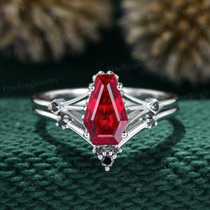 Puede incluir: Un anillo de plata con una gran piedra preciosa roja de forma octogonal. El anillo tiene un diseño delicado e intrincado con piedras preciosas negras más pequeñas.