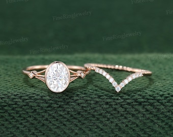 May include: A rose gold engagement ring with an oval-cut center stone and a matching chevron-shaped wedding band. The engagement ring features small accent stones on the band. The rings are set against a dark green background.