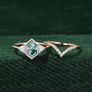 May include: A rose gold engagement ring set with a green moss agate gemstone in a hexagonal setting. The ring is flanked by two smaller triangular diamonds. The set also includes a matching rose gold band with a V-shaped row of diamonds.