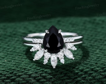 May include: A pear-shaped black diamond engagement ring set with a delicate band and a halo of smaller diamonds. The ring is set in white gold.